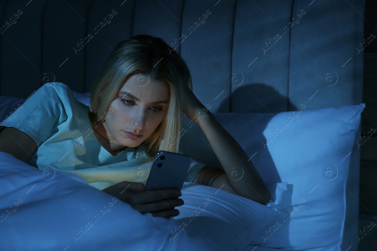 Photo of Young woman using smartphone in bed at night. Nomophobia and sleeping disorder problem