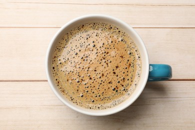 Cup of aromatic coffee on light wooden table, top view