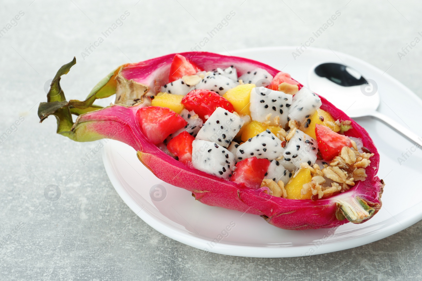 Photo of Yummy pitahaya boat with mango, granola and strawberry on light grey table, closeup