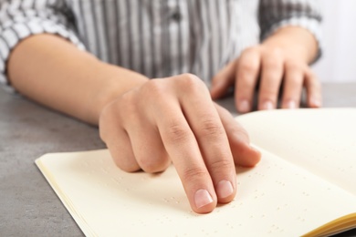 Photo of Blind person reading book written in Braille at table, closeup