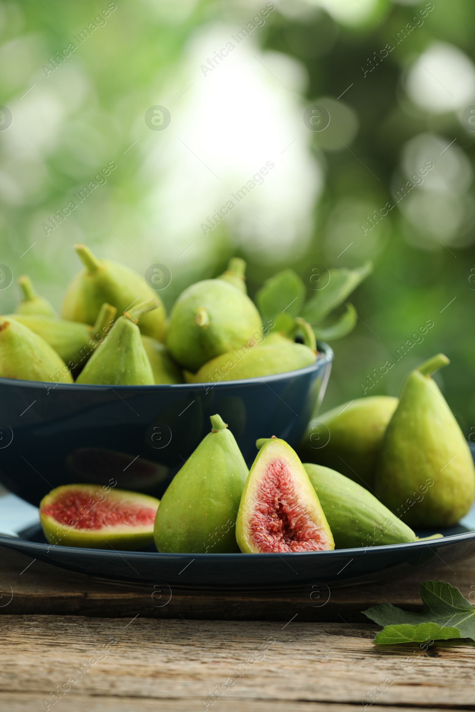 Photo of Cut and whole green figs on wooden table against blurred background, space for text