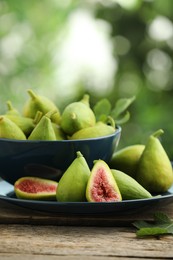 Photo of Cut and whole green figs on wooden table against blurred background, space for text