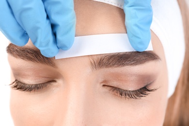 Photo of Young woman having professional eyebrow correction procedure in beauty salon