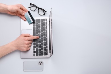 Online payment. Man with laptop, smartphone and credit card on light grey background, top view. Space for text