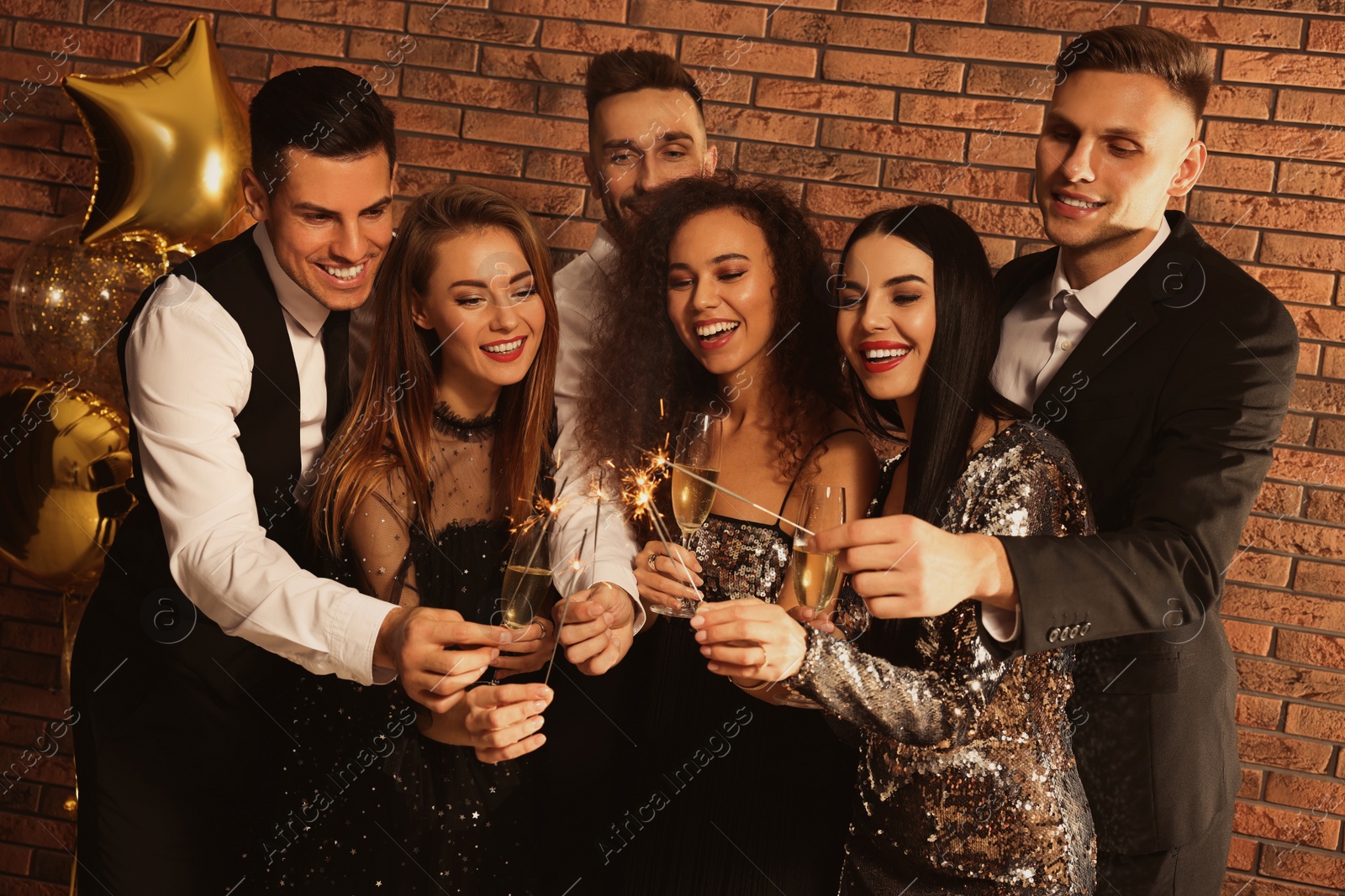 Photo of Happy friends with glasses of sparkling wine and sparklers celebrating New Year indoors