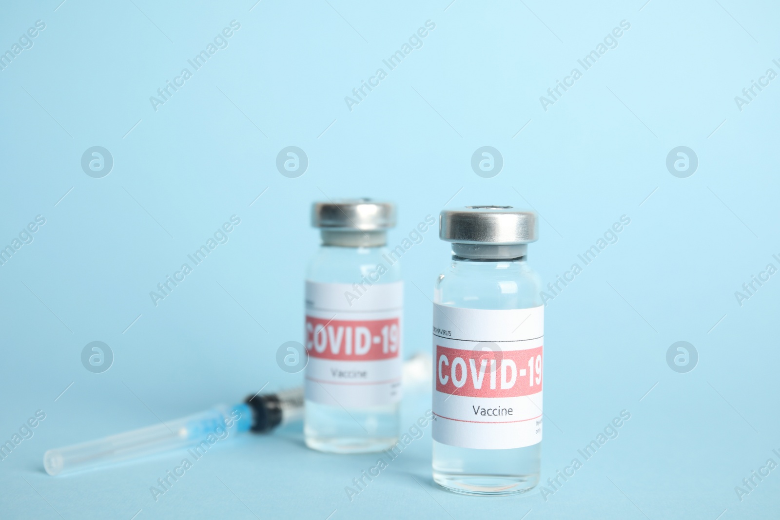 Photo of Vials with coronavirus vaccine and syringe on light blue background