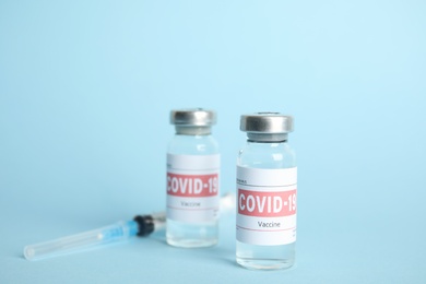 Vials with coronavirus vaccine and syringe on light blue background