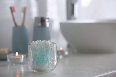 Photo of Glass holder with cotton buds on white countertop in bathroom. Space for text
