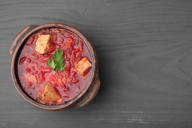 Photo of Tasty borscht in bowl on grey wooden table, top view. Space for text
