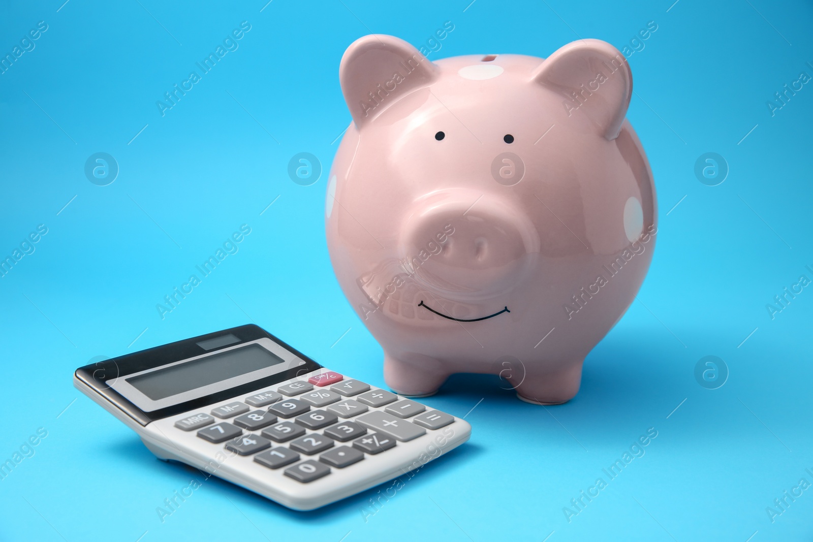 Photo of Piggy bank and calculator on light blue background