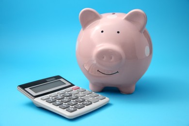 Photo of Piggy bank and calculator on light blue background