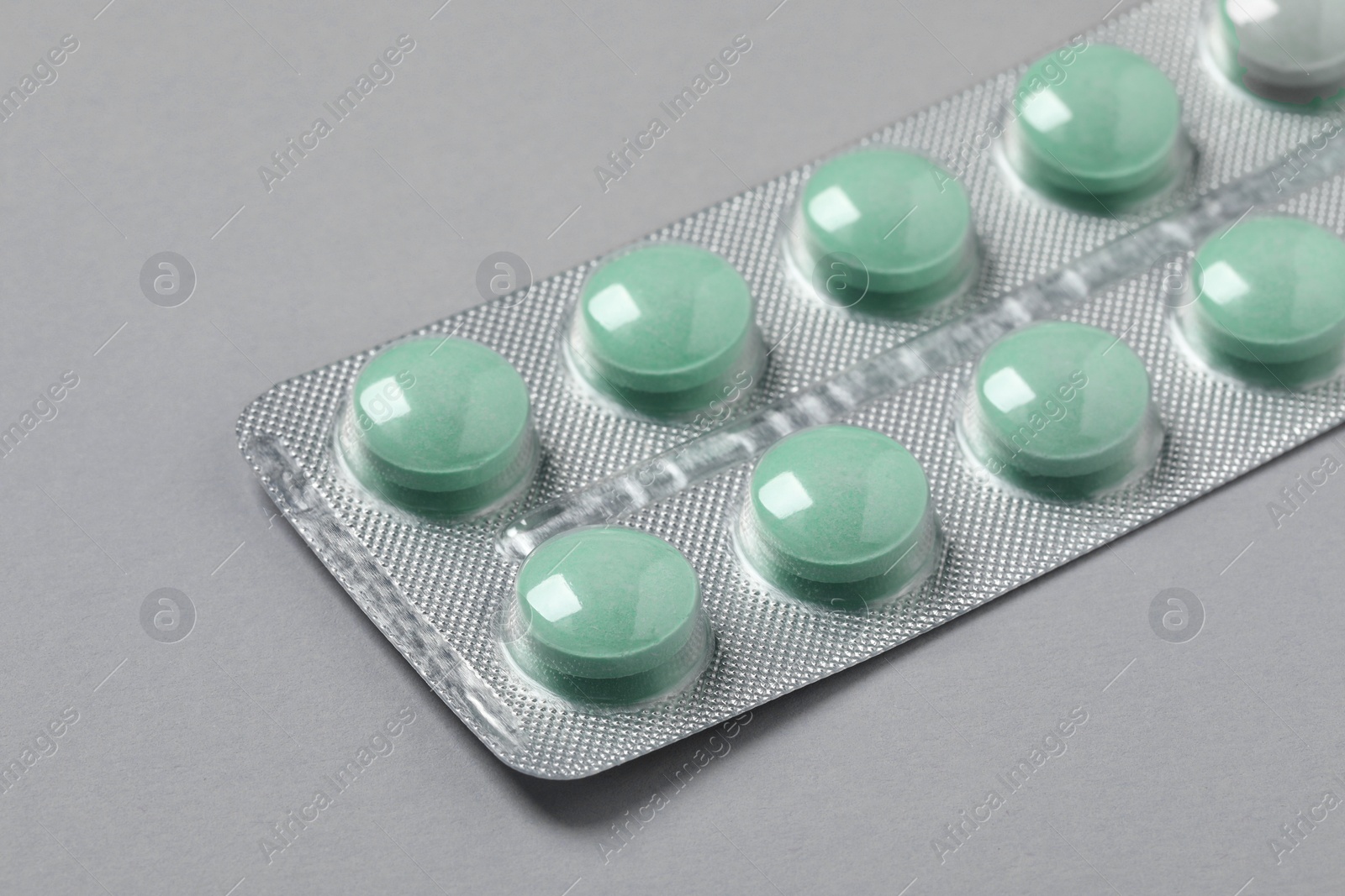 Photo of Green pills in blister on grey background, closeup