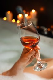 Photo of Woman drinking wine while taking bubble bath, closeup. Romantic atmosphere