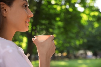 Beautiful young woman with drink in park on sunny day, space for text