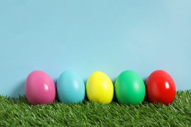Photo of Bright Easter eggs on green grass against light blue background