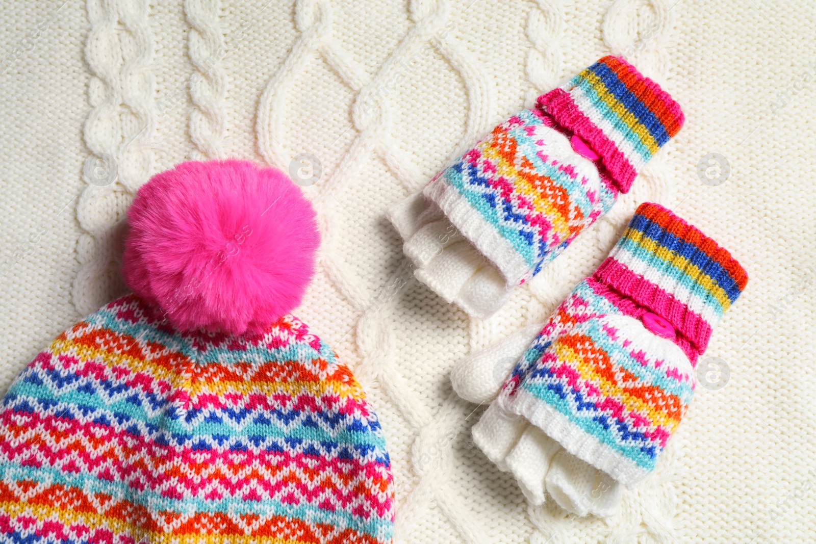 Photo of Warm hat and mittens on white knitted fabric, flat lay