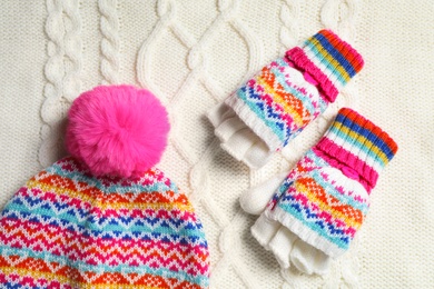 Warm hat and mittens on white knitted fabric, flat lay