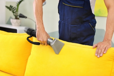 Photo of Dry cleaning worker removing dirt from sofa indoors