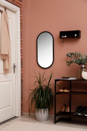 Photo of Hallway interior with green plants and wooden hanger for keys on pale pink wall