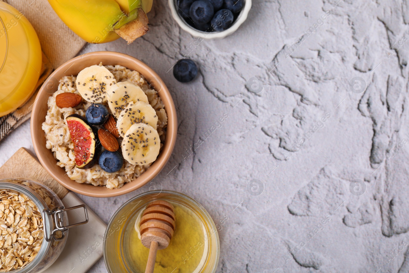 Photo of Bowl of oatmeal with blueberries, almonds, banana and fig pieces on white textured table, flat lay. Space for text