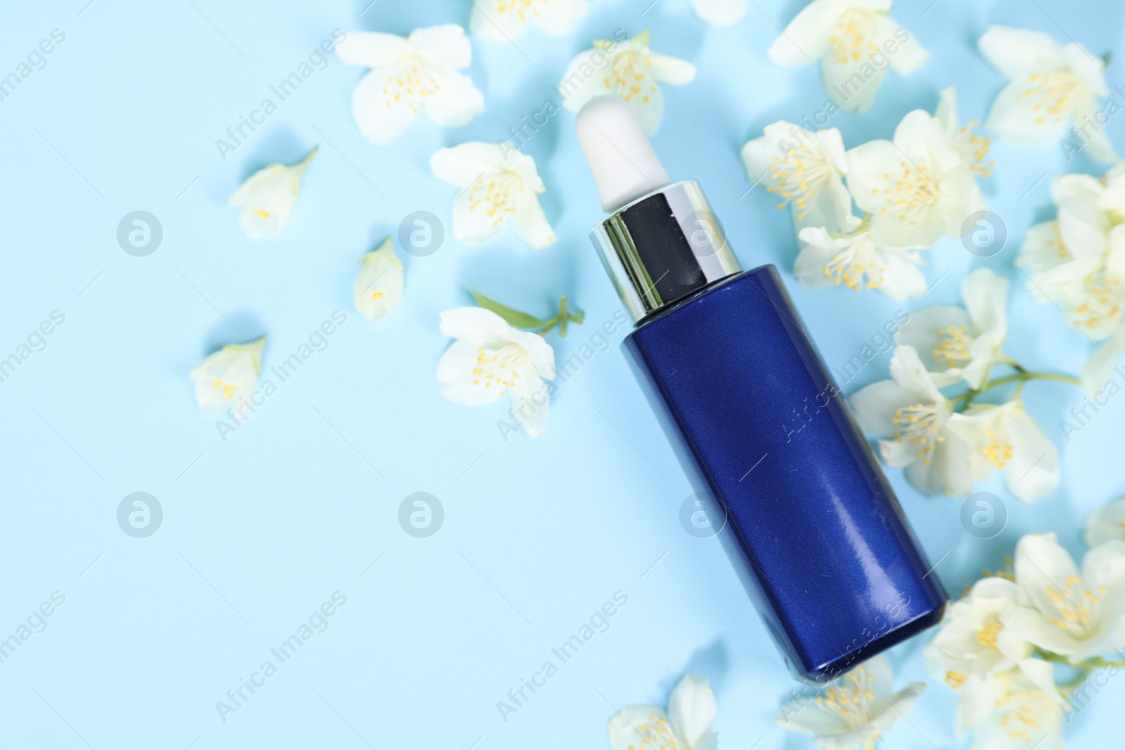 Photo of Essential oil in bottle and beautiful jasmine flowers on light blue background, flat lay. Space for text