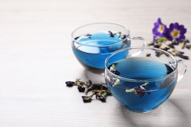 Glass cups of organic blue Anchan on white wooden table, space for text. Herbal tea