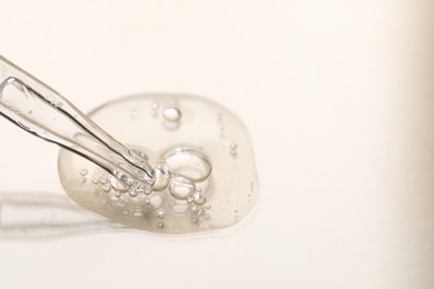 Photo of Glass pipette and transparent liquid on beige background, closeup. Space for text