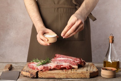 Man salting fresh raw meat on table against grey background, closeup