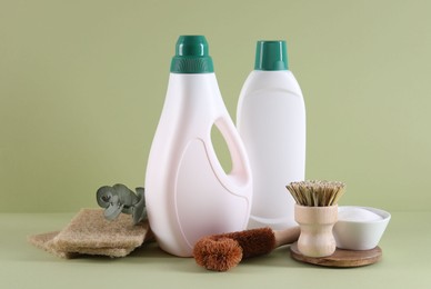 Bottles of cleaning product, sponges, baking soda and brushes on light green background