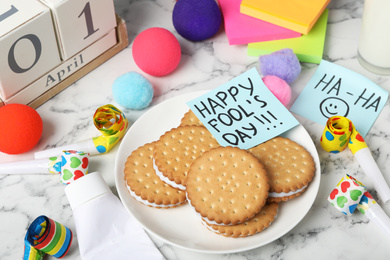 Photo of Cookies with toothpaste and HAPPY FOOL'S DAY note on white marble table. April holiday