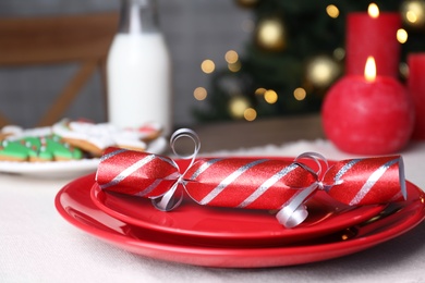 Red plate with Christmas cracker on table, closeup