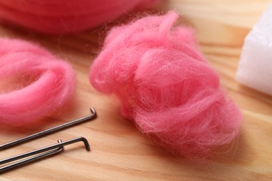Pink felting wool and needles on wooden table, closeup