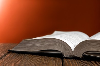 Photo of Open Bible on wooden table against brown background, closeup. Space for text
