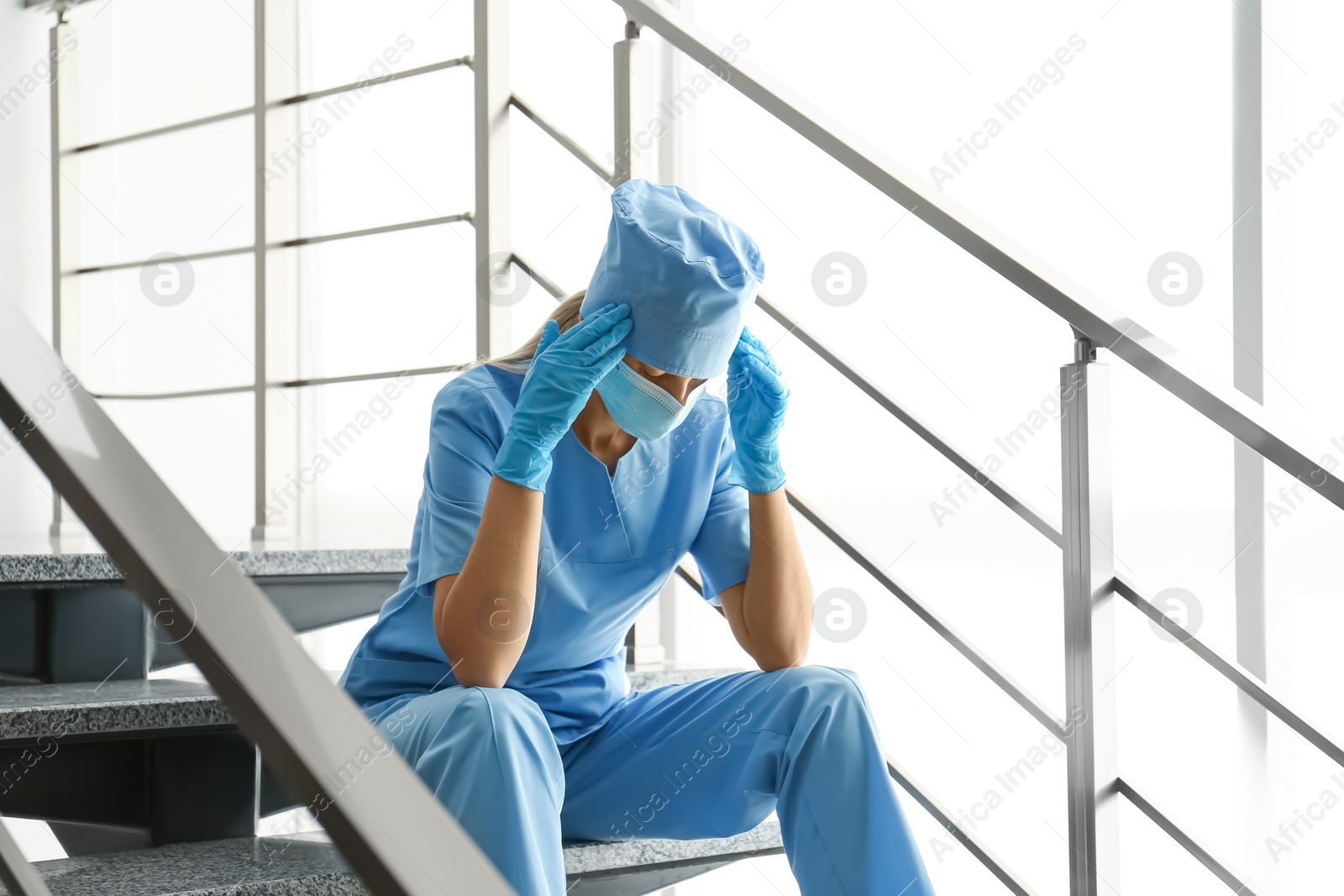 Photo of Exhausted doctor sitting on stairs in hospital. Stress of health care workers during COVID-19 pandemic