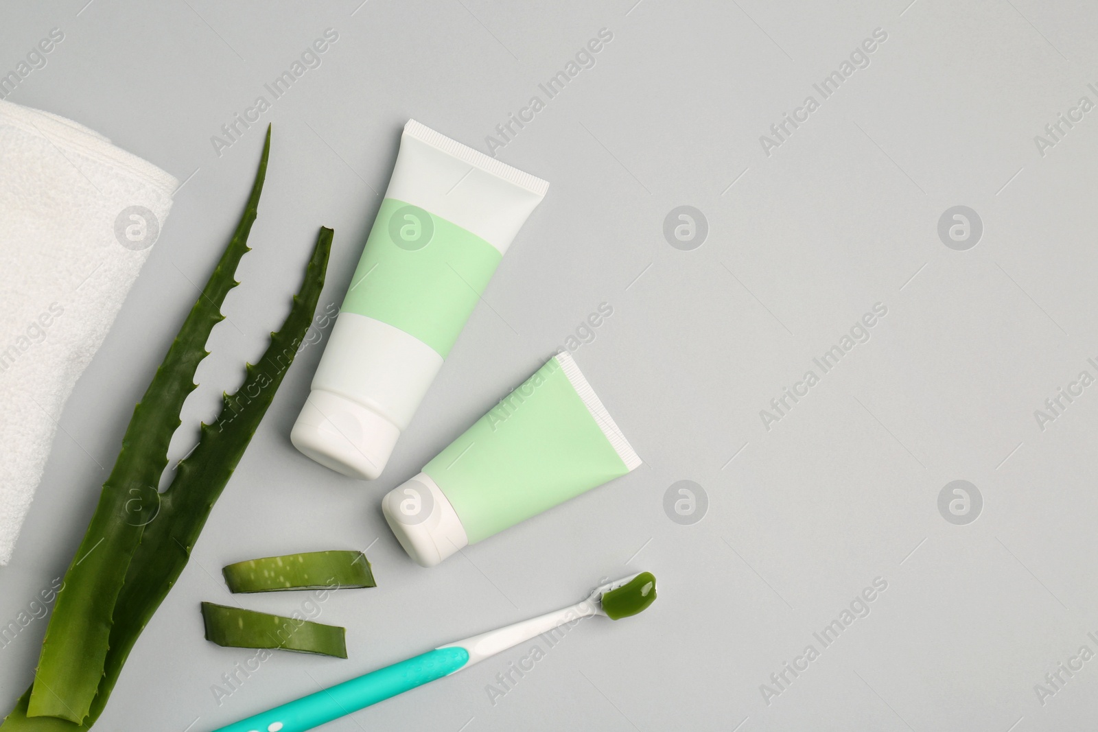 Photo of Tubes of toothpaste, toothbrush and fresh aloe on light grey background, flat lay. Space for text