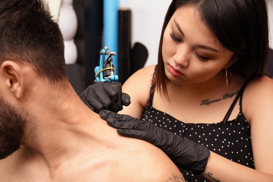 Photo of Professional artist making tattoo with machine in salon