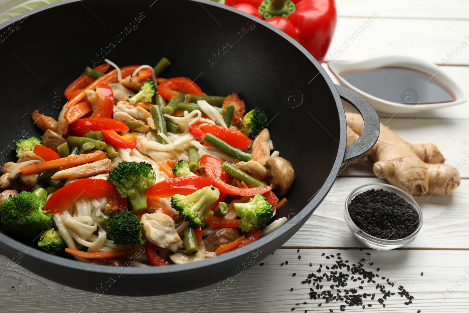 Photo of Stir fried noodles with mushrooms, chicken and vegetables in wok on white wooden table, closeup