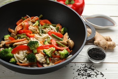 Stir fried noodles with mushrooms, chicken and vegetables in wok on white wooden table, closeup