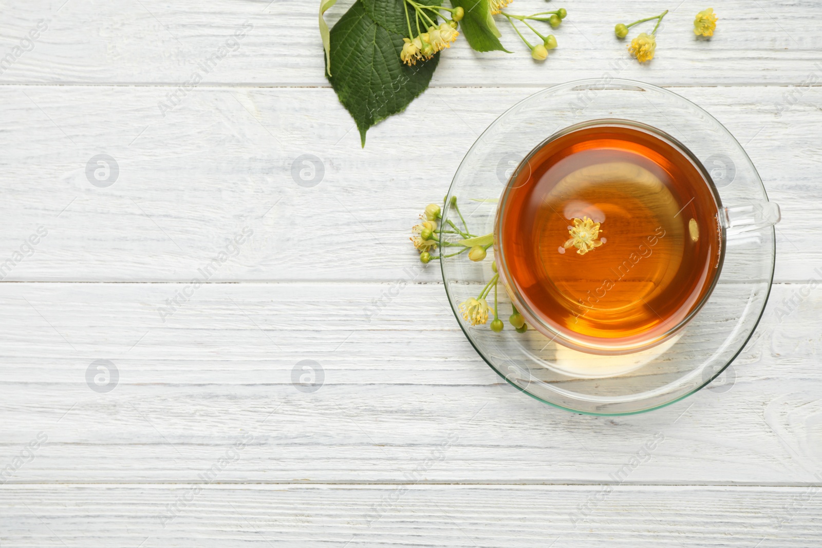 Photo of Cup of tea and linden blossom on white wooden table, flat lay. Space for text