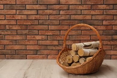 Photo of Wicker basket with firewood near brick wall indoors, space for text