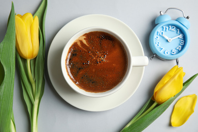 Photo of Aromatic morning coffee, alarm clock and beautiful flowers on light grey background, flat lay