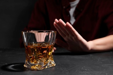 Photo of Alcohol addiction. Woman refusing glass of whiskey at dark textured table, closeup