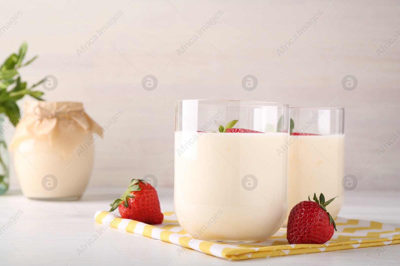 Photo of Tasty yogurt and strawberries in glasses on white wooden table, closeup. Space for text