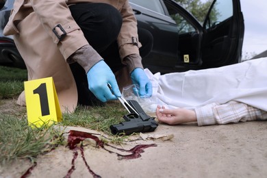 Photo of Investigator in protective gloves working at crime scene with dead body outdoors, closeup