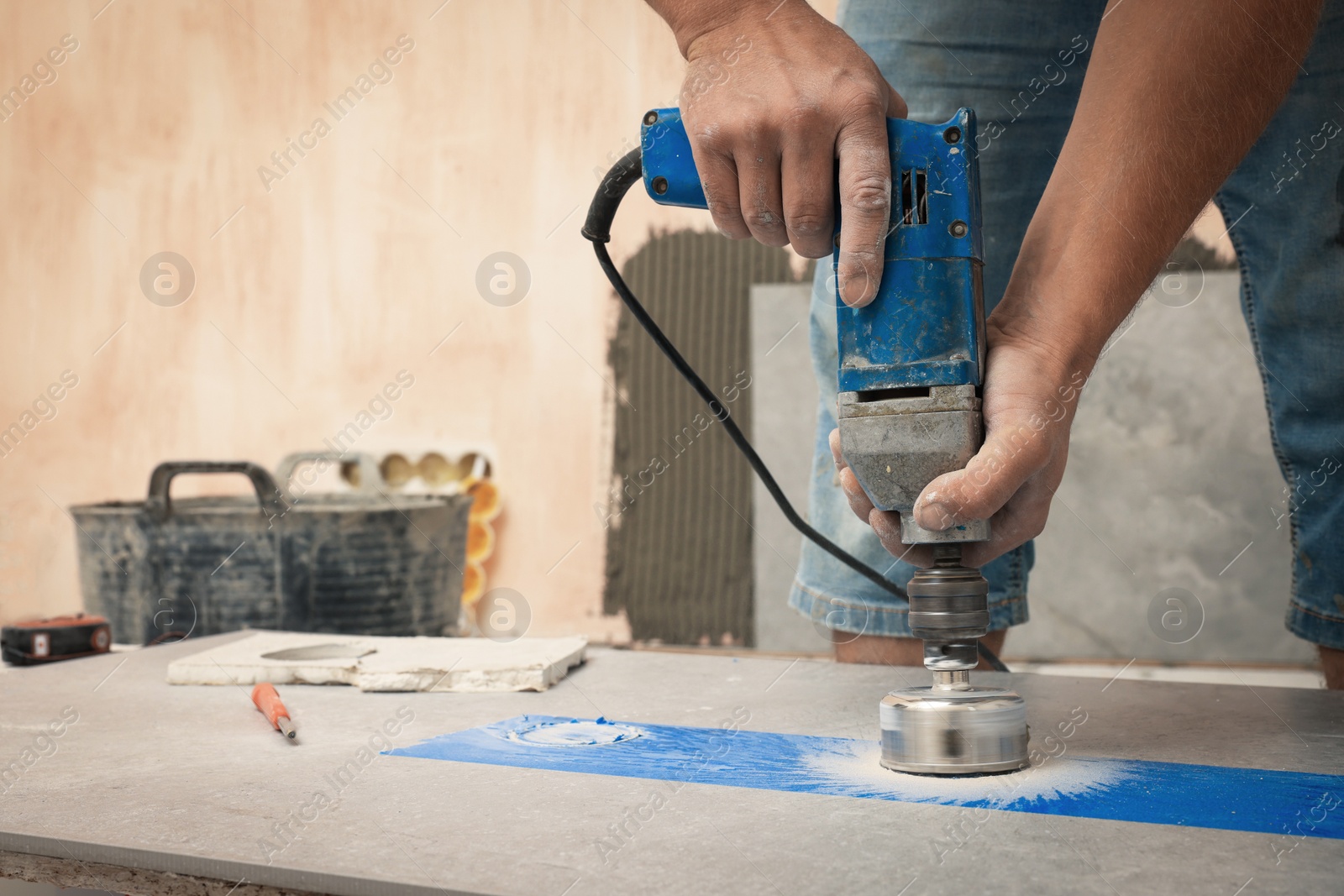 Photo of Worker making socket hole in tile indoors, closeup