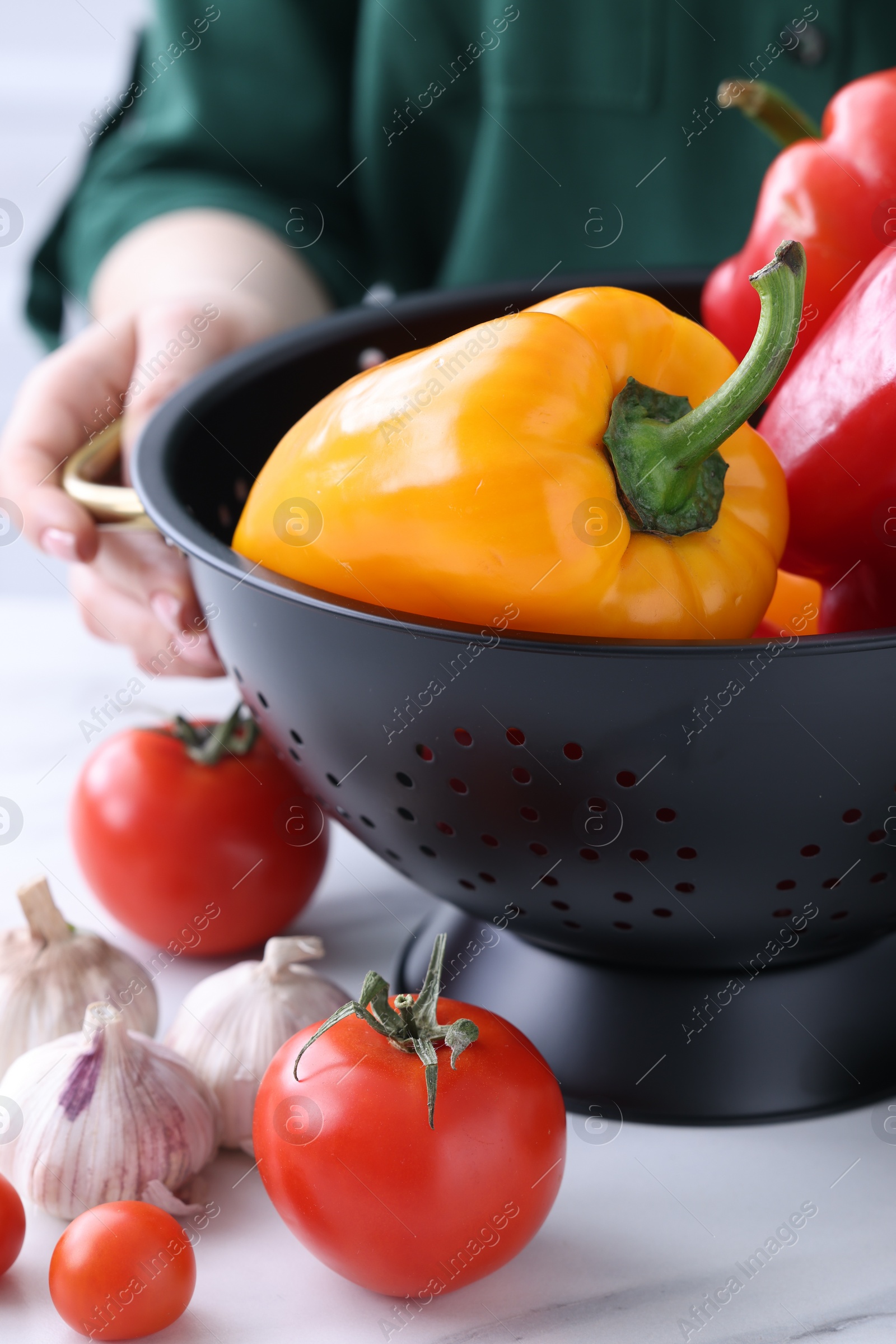 Photo of Woman holding black colander with bell pepper at white table indoors, closeup