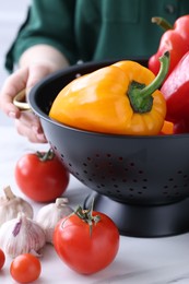 Woman holding black colander with bell pepper at white table indoors, closeup