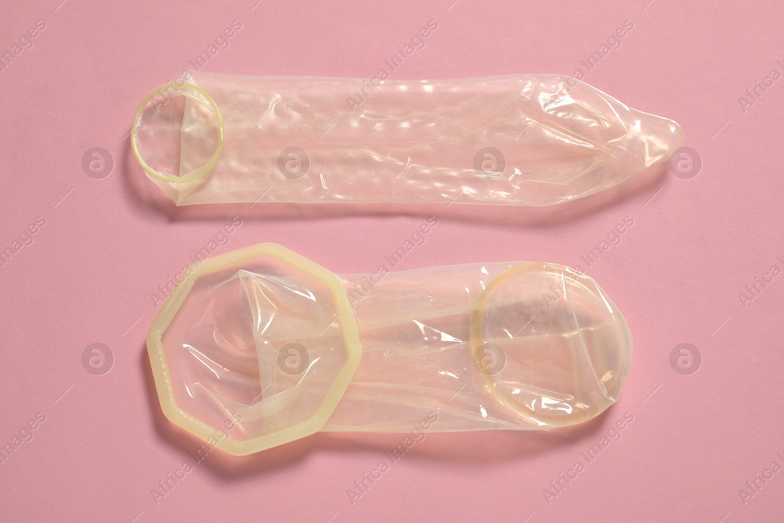 Photo of Unrolled female and male condoms on light pink background, flat lay. Safe sex