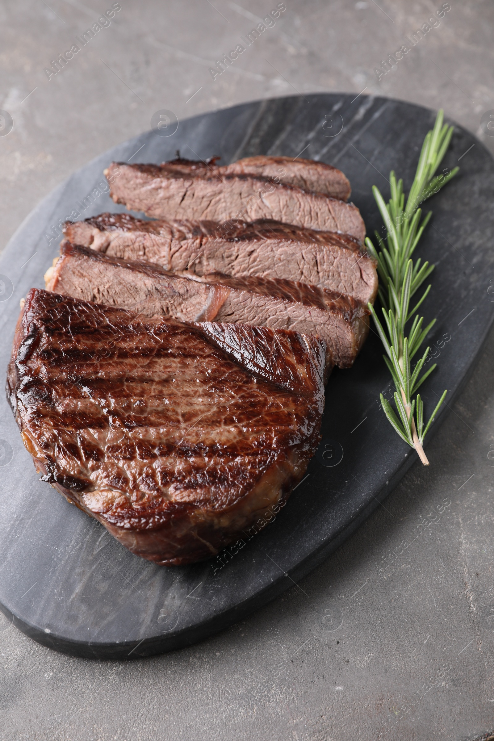 Photo of Delicious fried beef meat with rosemary on grey textured table