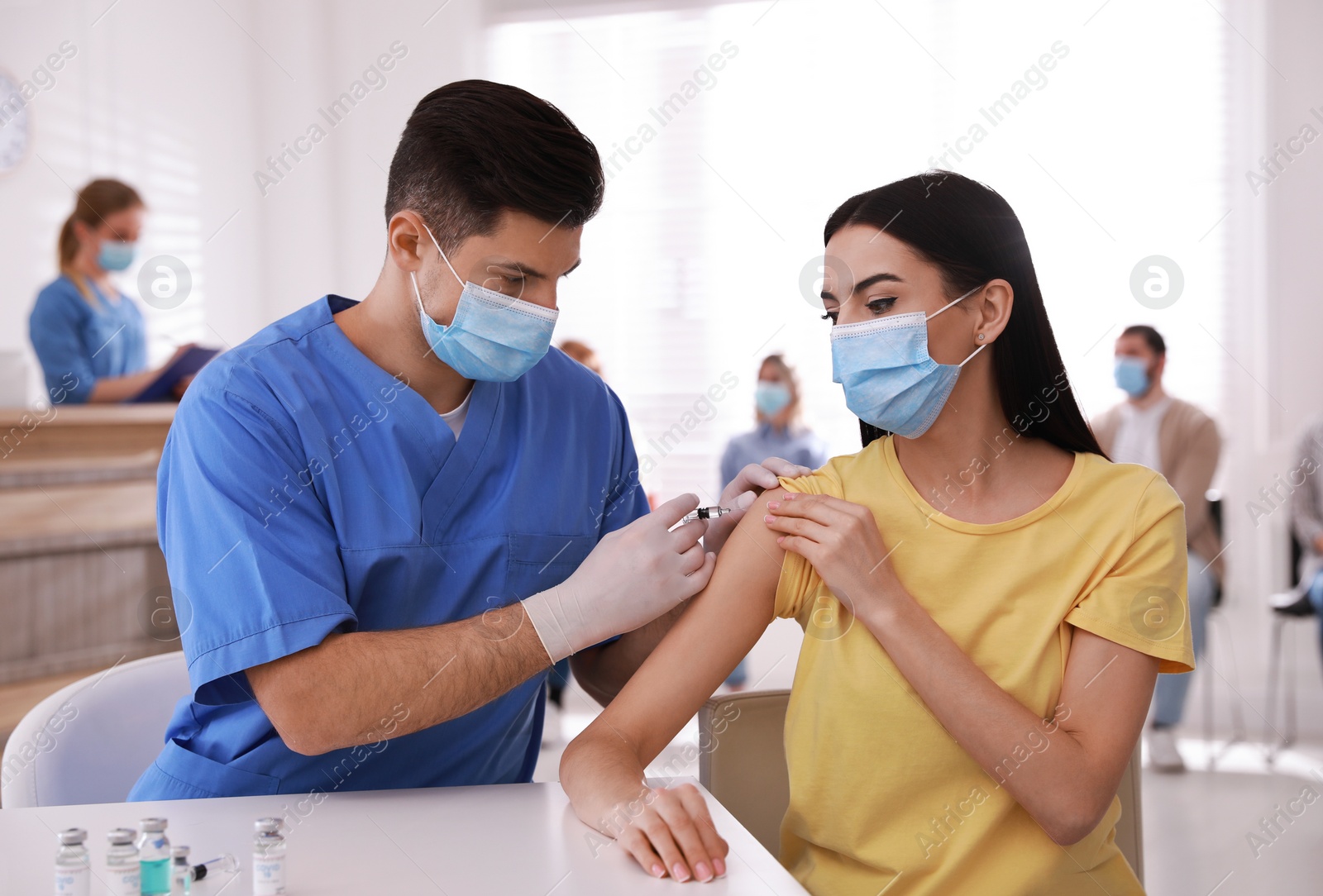 Photo of Doctor giving injection to patient while other waiting in line at hospital. Vaccination campaign